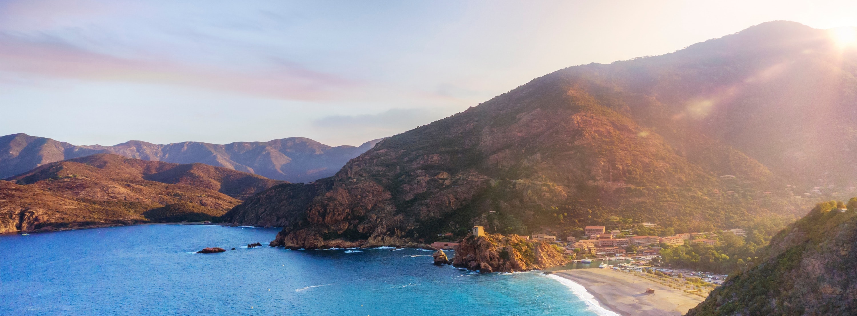 Landscape image of a sunset in Corsica, with the sea in the foreground and mountains in the background